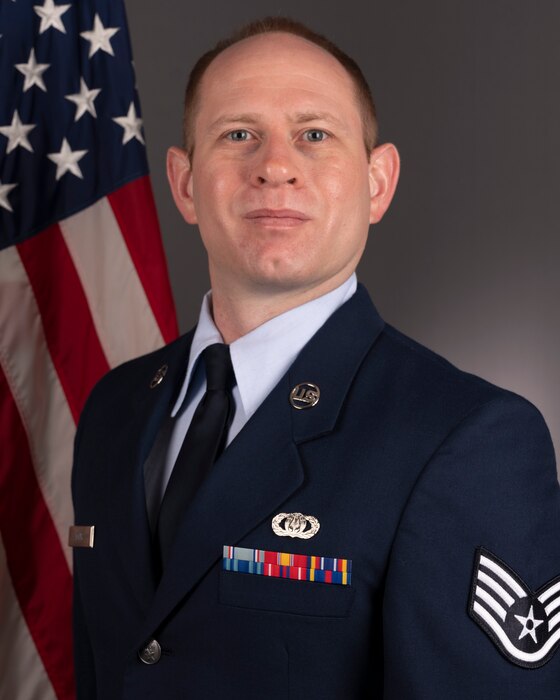 Official Photo of SSgt Daniel Dyar, percussionist with Rhythm in Blue and the Concert Band, two of six ensembles in the Heritage of America Band, Langley AFB, VA.  SSgt Dyar is wearing blue service dress in front of the American flag.