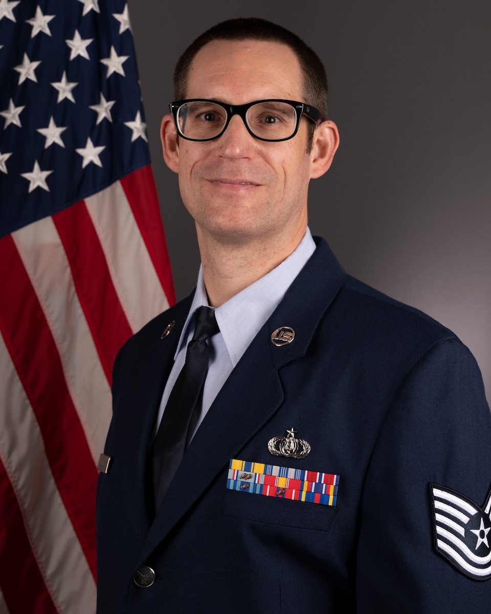 Official Photo of TSgt Craig Buying, clarinetist with the American Clarinet Quartet and the Concert Band, two of six ensembles in the Heritage of America Band, Langley AFB, VA.  TSgt Buying is wearing blue service dress in front of the American flag.