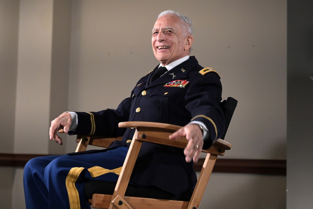 A man wearing a uniform grins as he sits back in a chair.