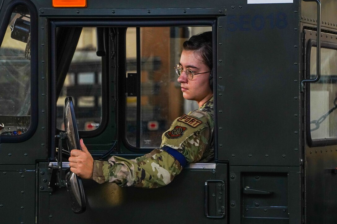 An airman looks in a mirror while sitting in the driver’s seat of a vehicle.