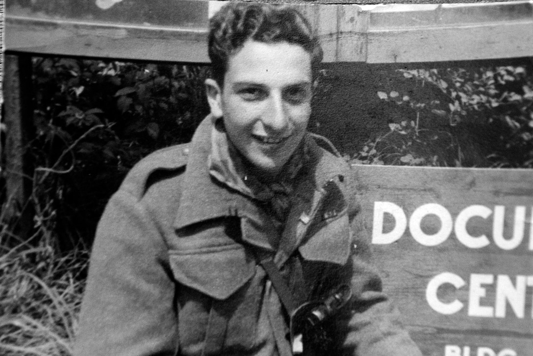 A soldier poses for a photo in front of a sign.
