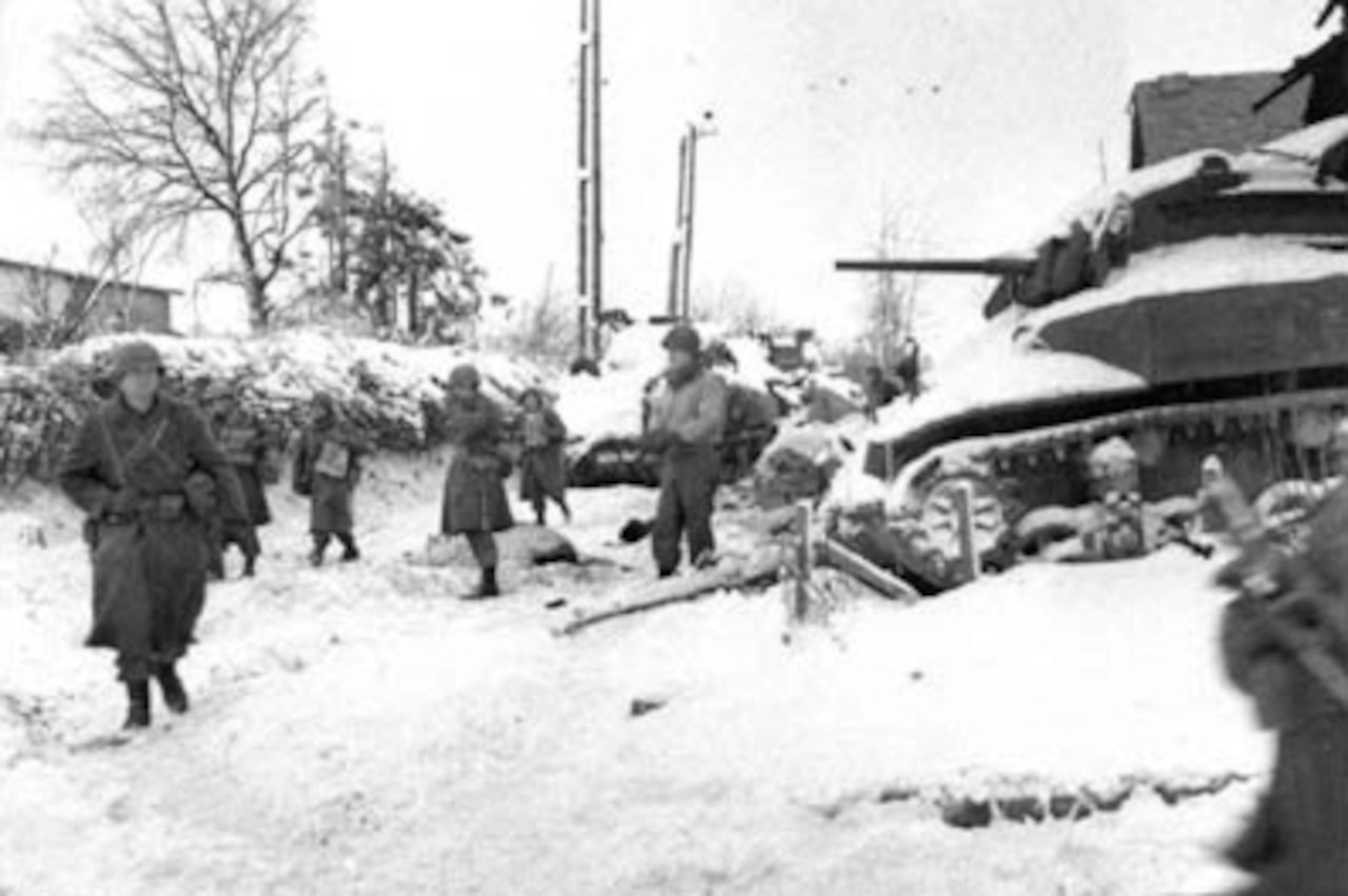 Soldiers walk through snow; a tank is to the right.