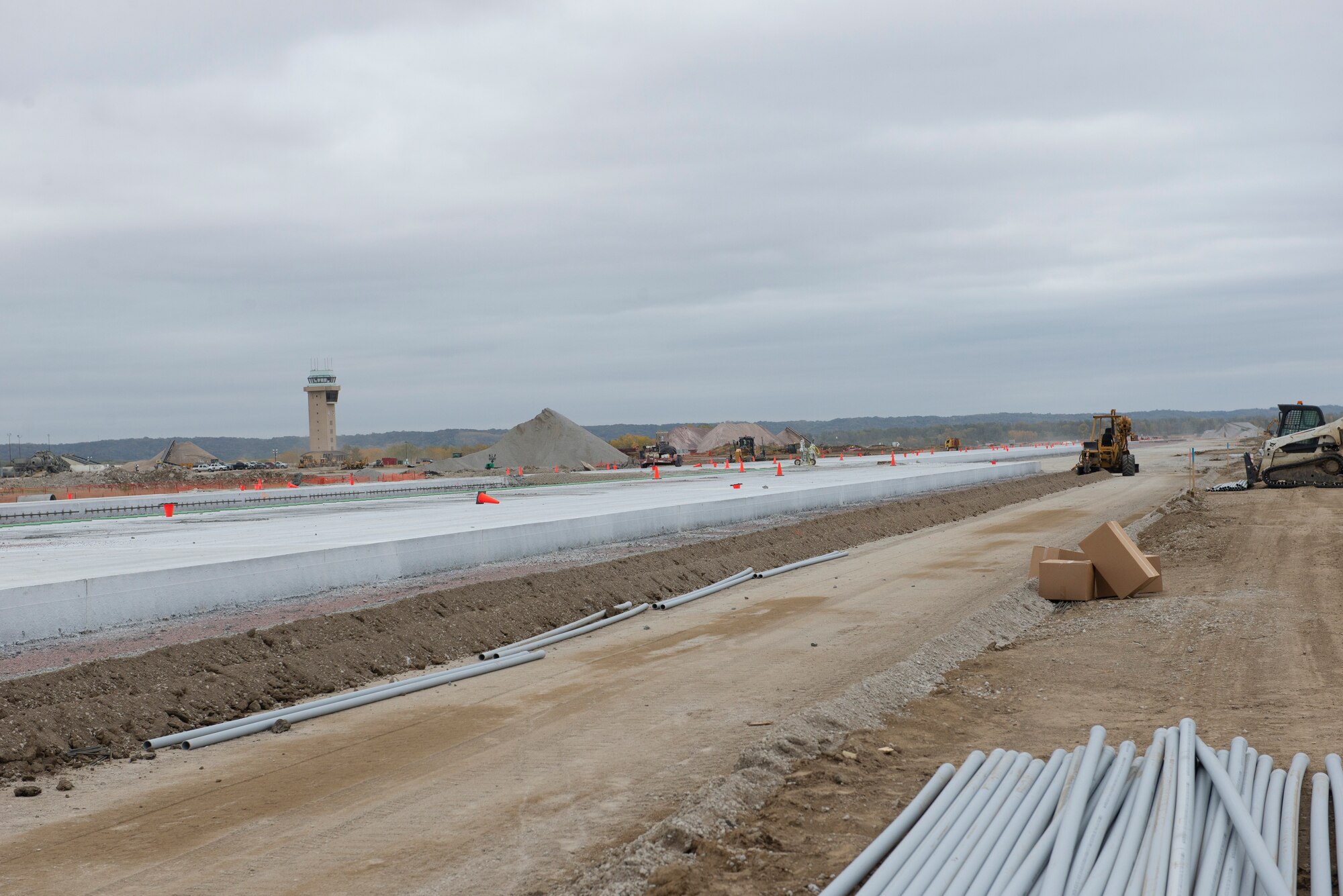 Long shot of construction site showing equipment, tools, dirt, and partial concrete runway