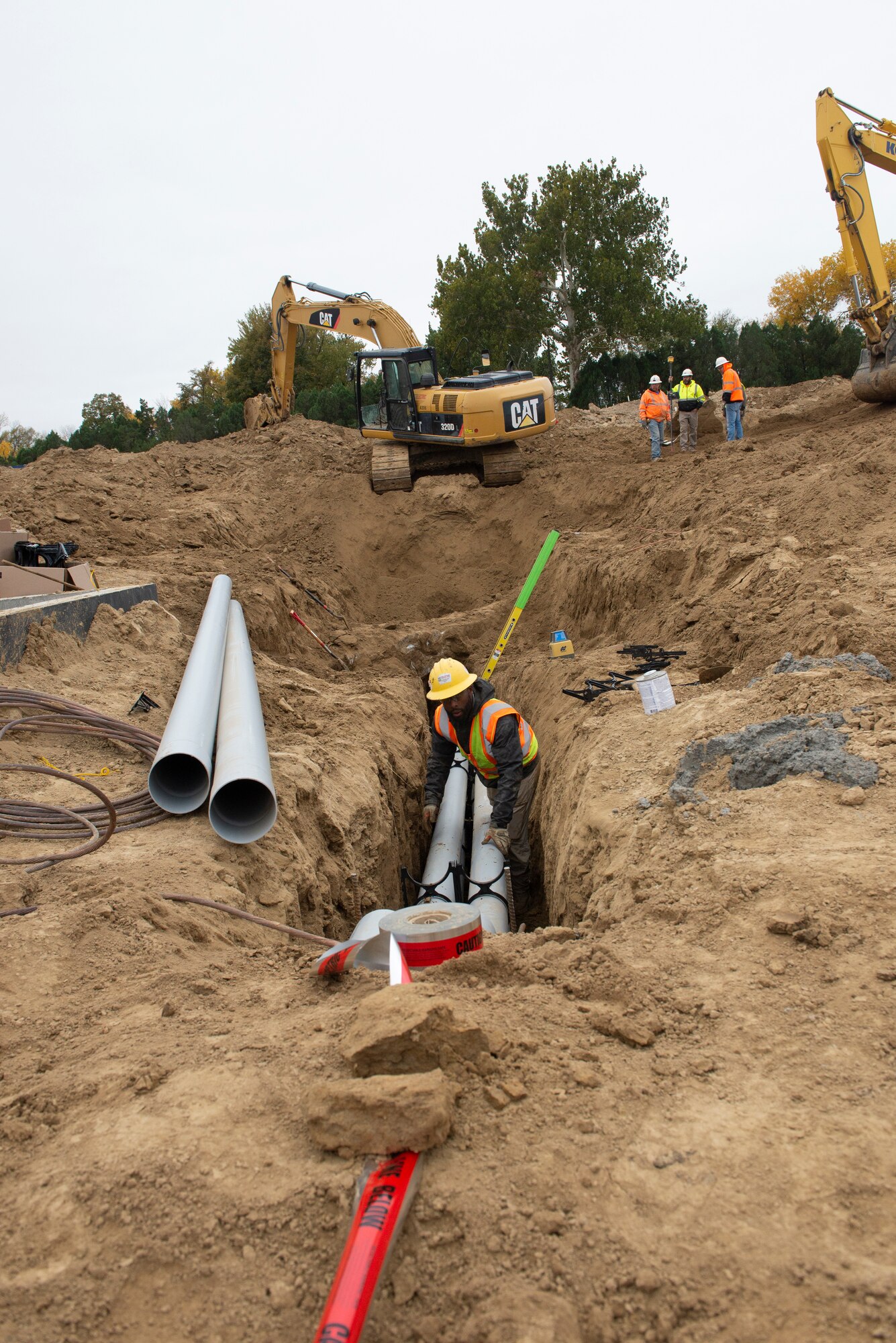 Construction worker in dirt trench with pipes