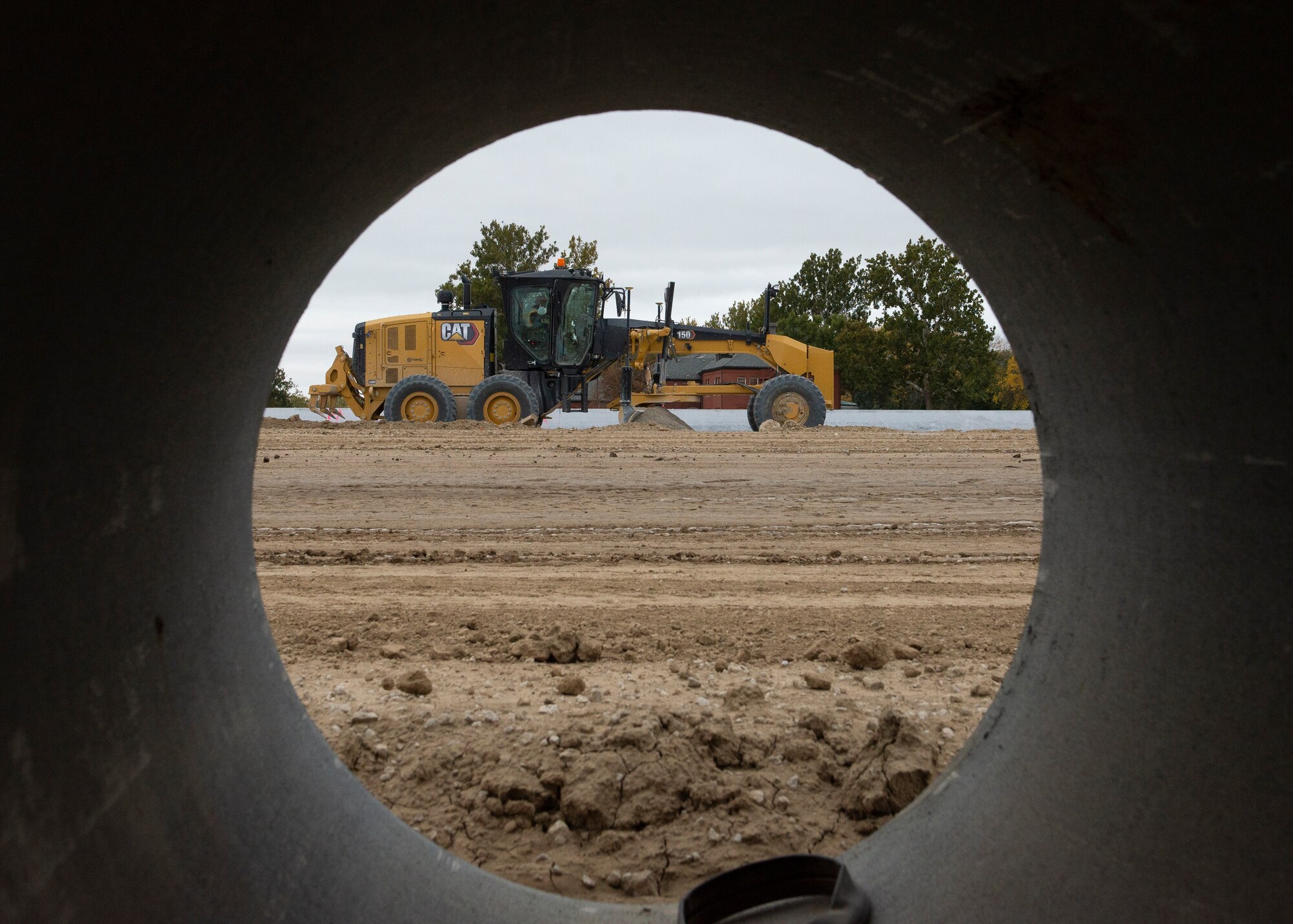 Picture of large yellow construction earth grader through concrete tube