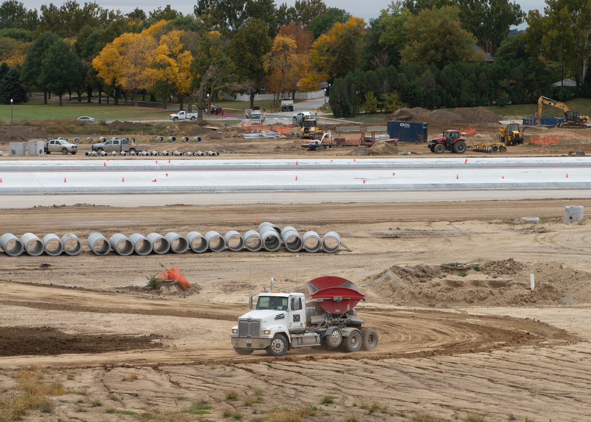 Far shot of semi-truck on dirt in front of newly laid concrete for new runway