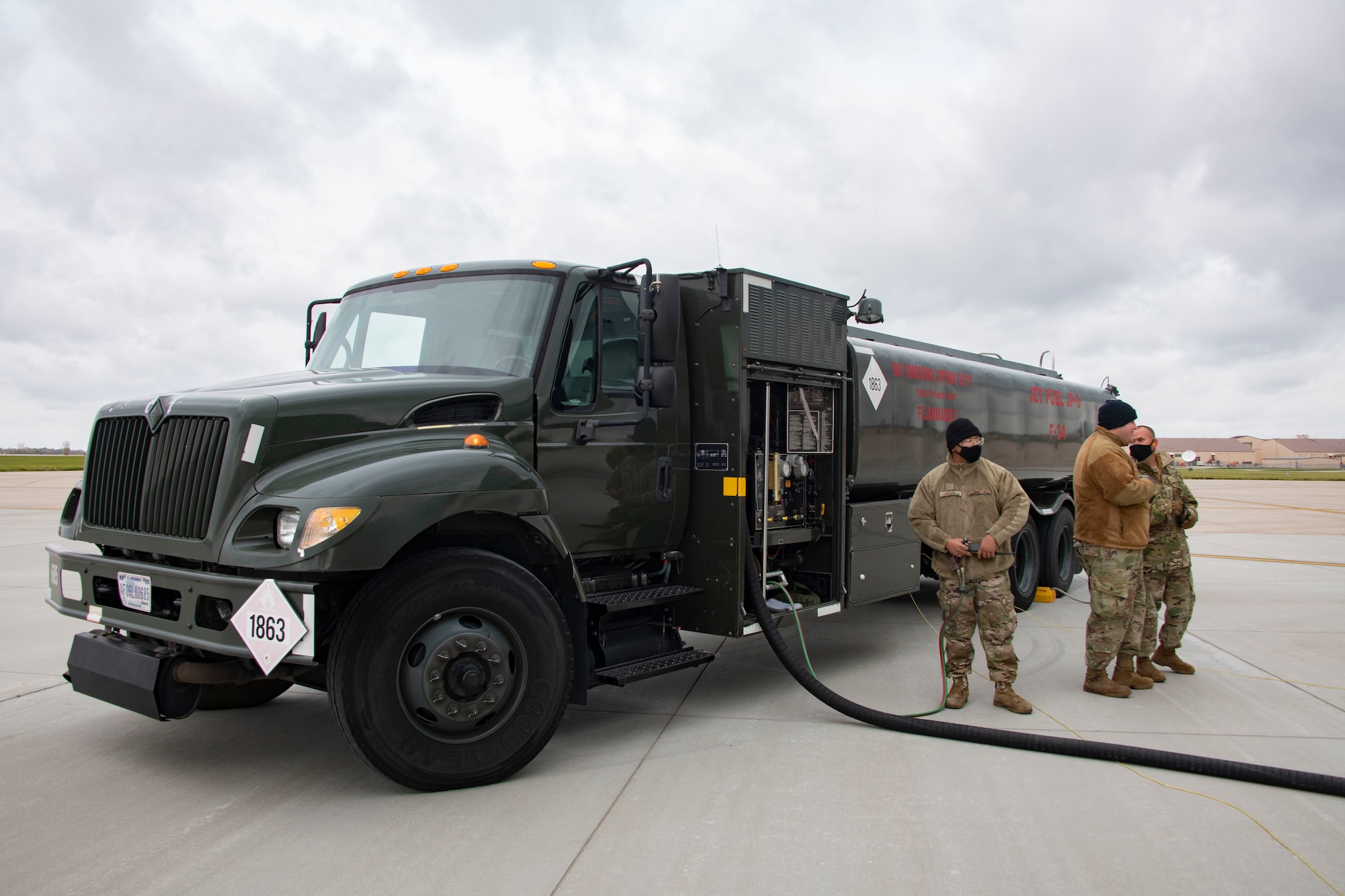 Three Airmen stand next to a refueling truck