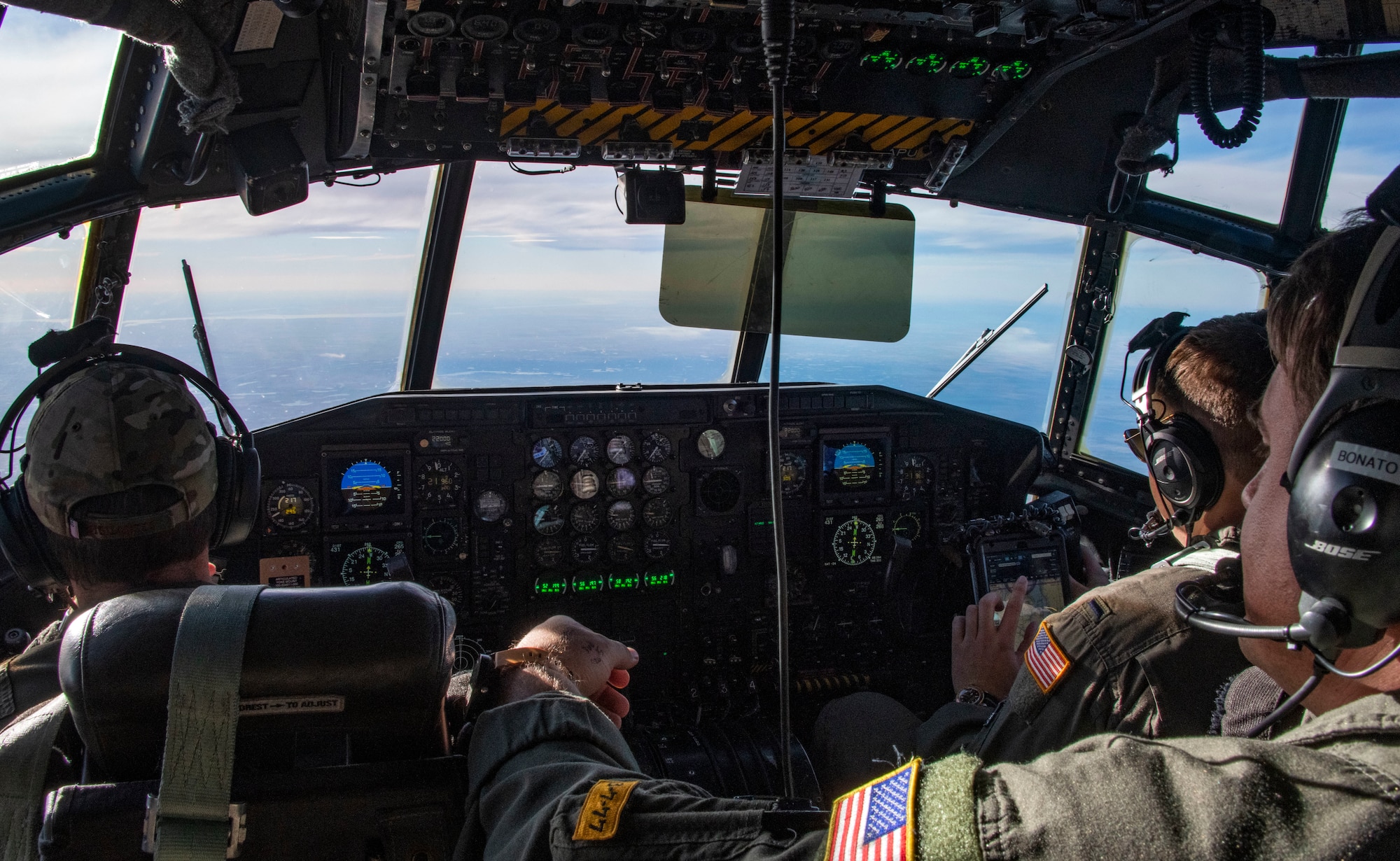 Three pilots look forward while sitting in the cockpit of a C-130