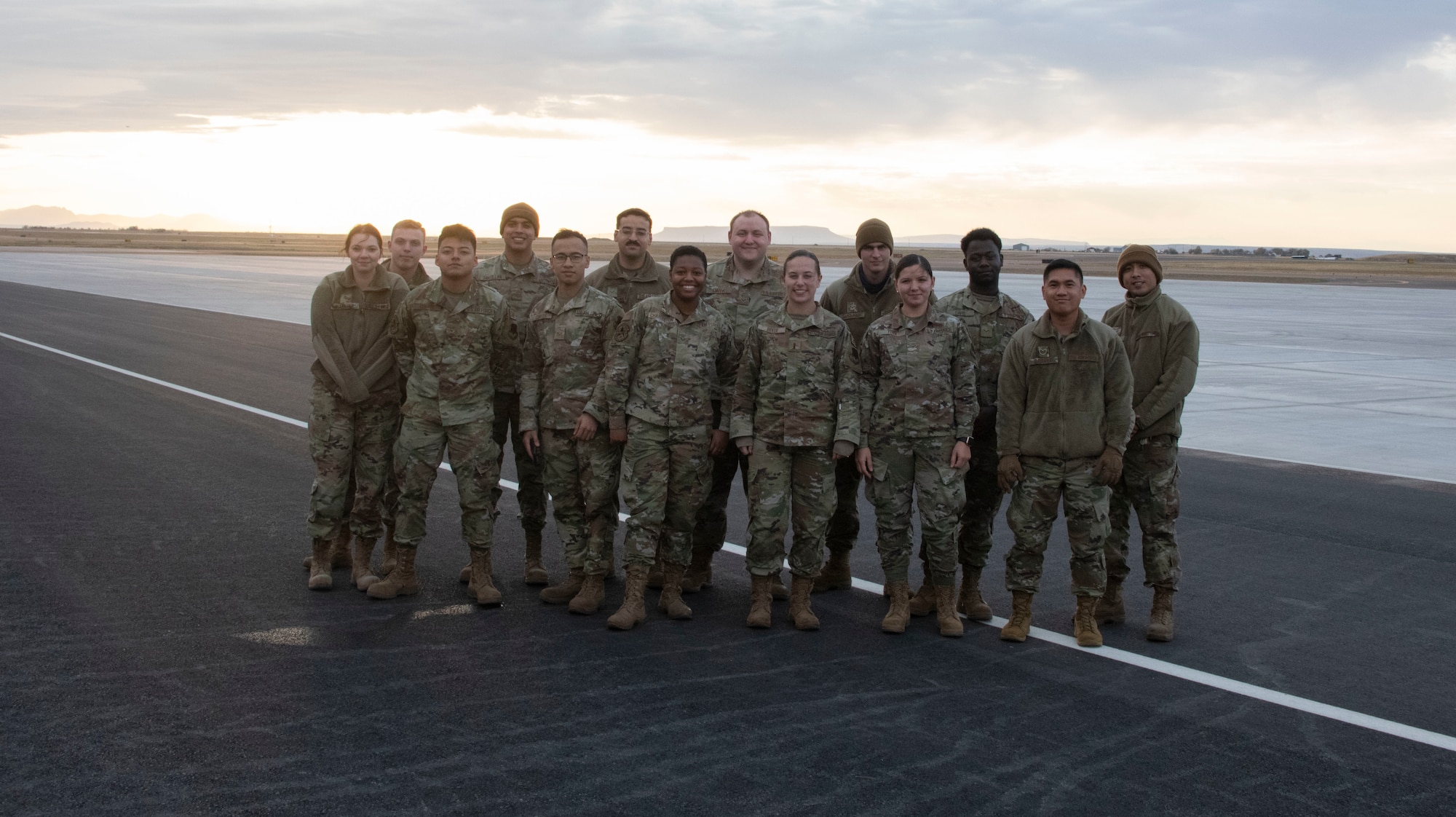 A group of Airmen smile for the camera while standing on the flight line