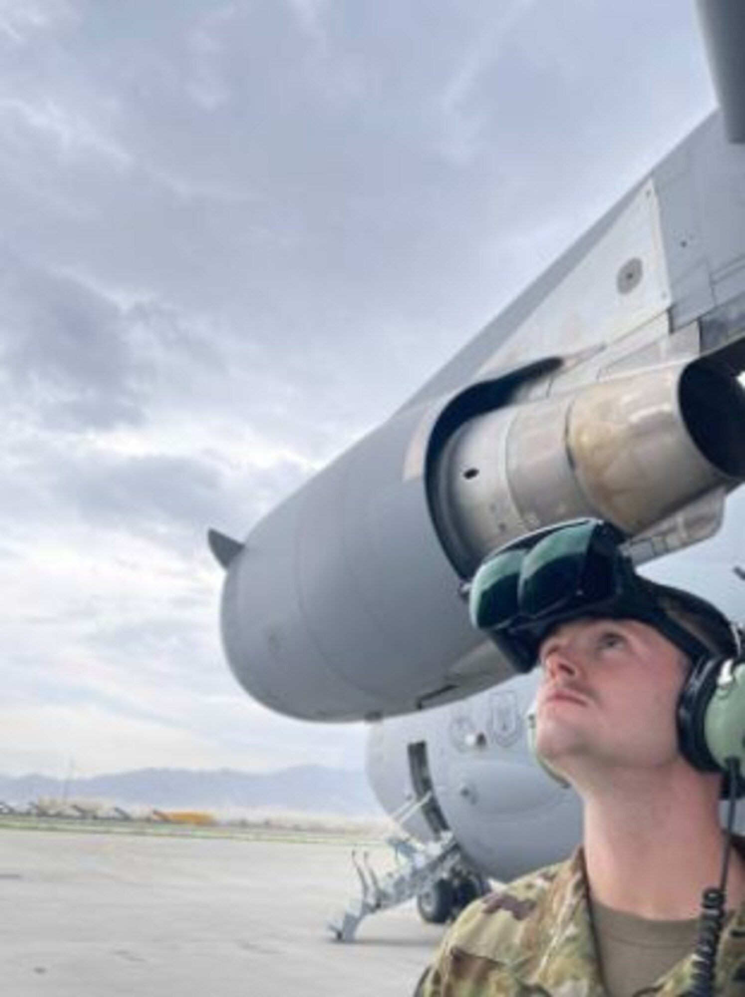 A uniformed Airman looks up at a plane on an overcast day with an AR headset on his head