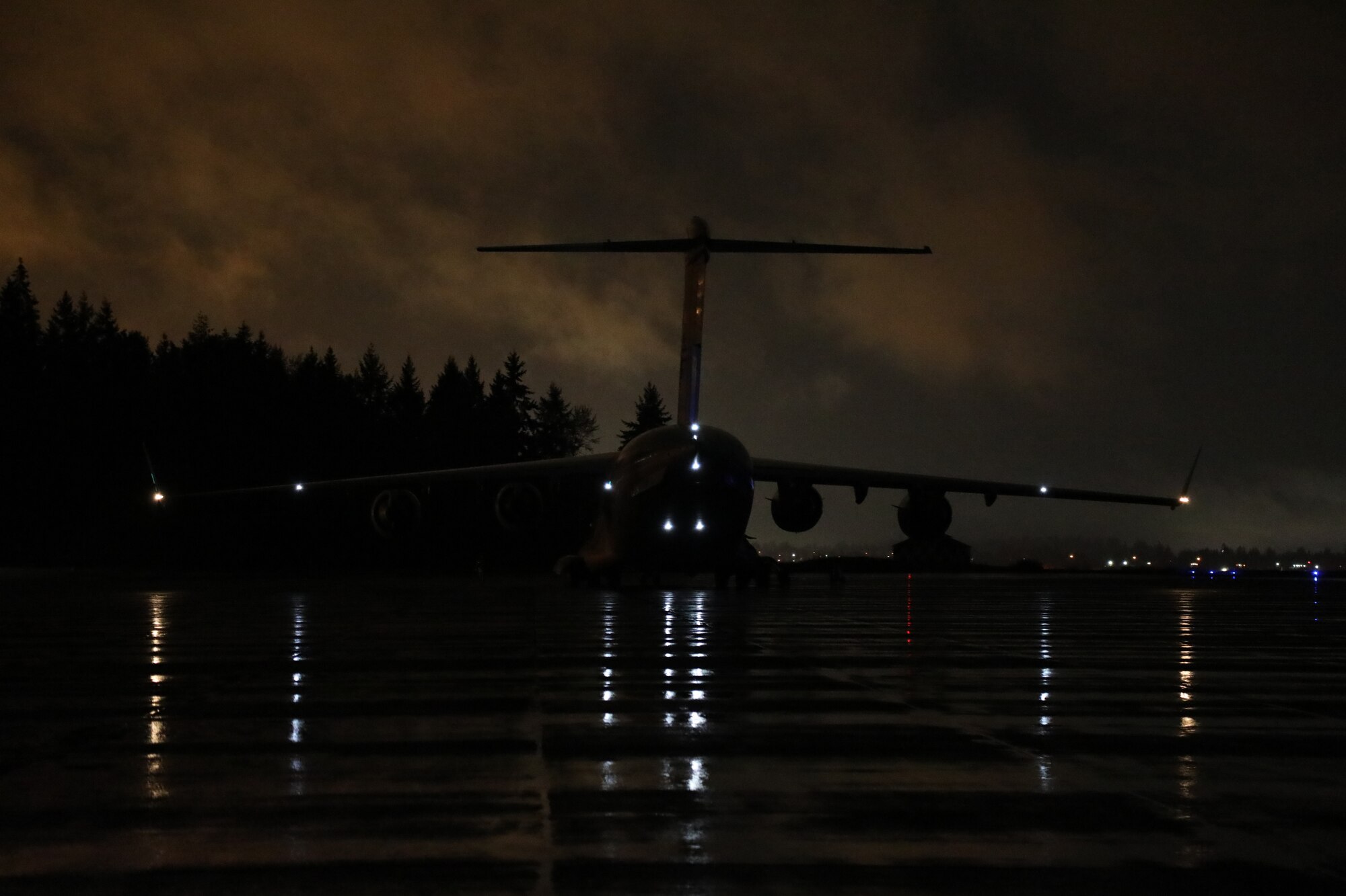 A C-17 Globemaster III sits on the flightline at night during Exercise Rainier War 21B at Joint Base Lewis-McChord, Washington, Nov.  3, 2021. Rainier War 21B exercises and evaluates the wing’s ability to employ the force and their ability to perform during wartime and/or contingency taskings in a high-intensity, wartime contested, degraded and operationally limited environment while supporting the contingency operations against a near-peer adversary in the U.S. Indo-Pacific Command area of responsibility. (U.S. Air Force photo by Senior Airman Christopher Sommers)