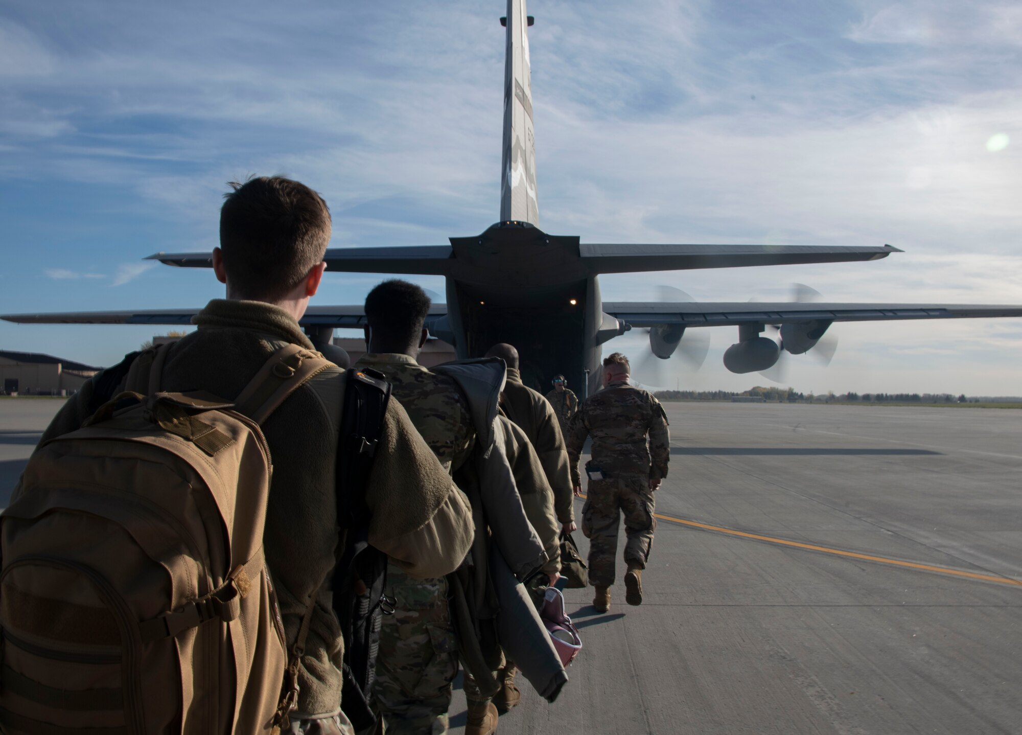 Airmen walk in a single file line into a C-130