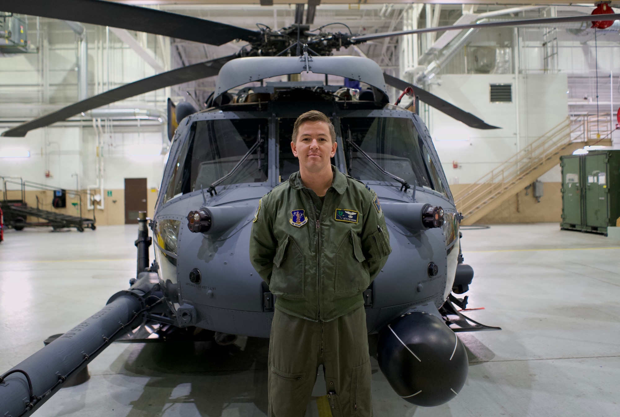 U.S. Air Force Captain Seth Peterson, a helicopter pilot assigned to the 210th Rescue Squadron, Joint Base Elemendorf-Richardson, Alaska, stands in front of an HH-60G Pave Hawk helicopter in a hanger at JBER Nov. 3, 2021. Capt. Peterson commissioned as an U.S. Air Force officer after serving as a U.S. Marine with the 4th Battalion.