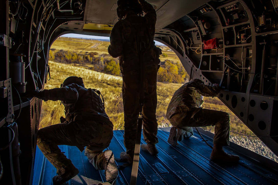 Three soldiers look out of the back of a helicopter.