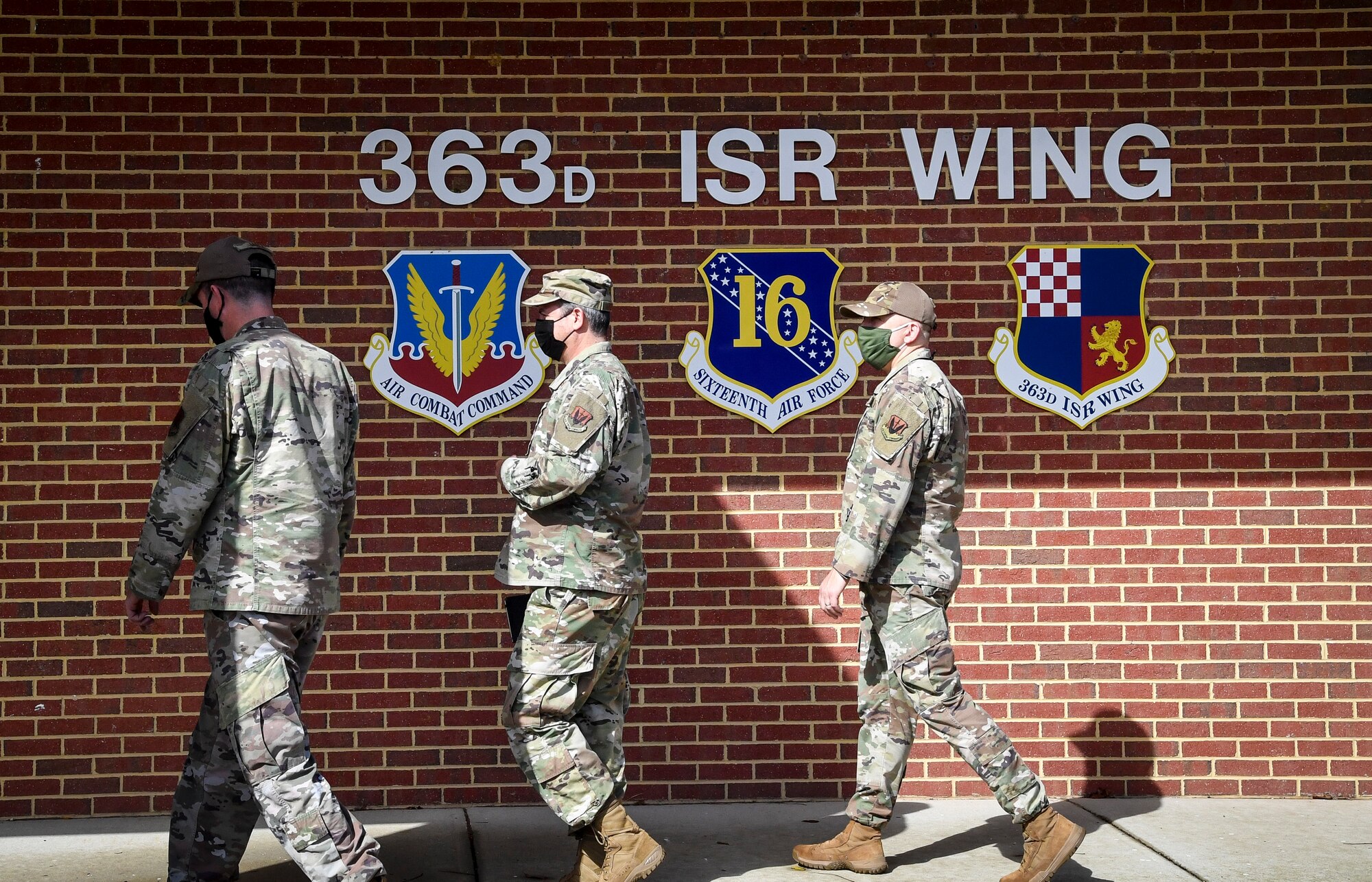 Three individuals walking across 363d Intelligence, Surveillance, and Reconnaissance Wing building sign.