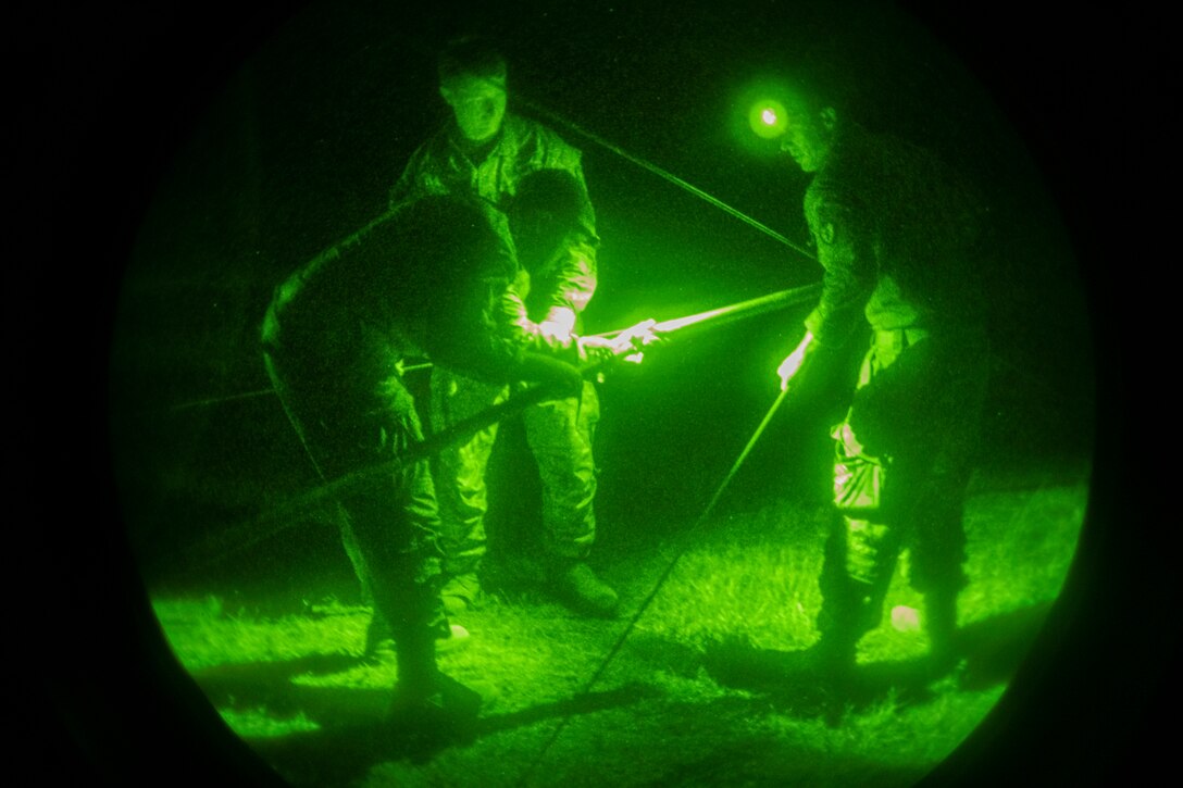 Three soldiers assemble a tent at night.