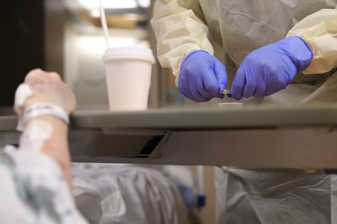 Gloved hands prepare a medication on a hospital table.