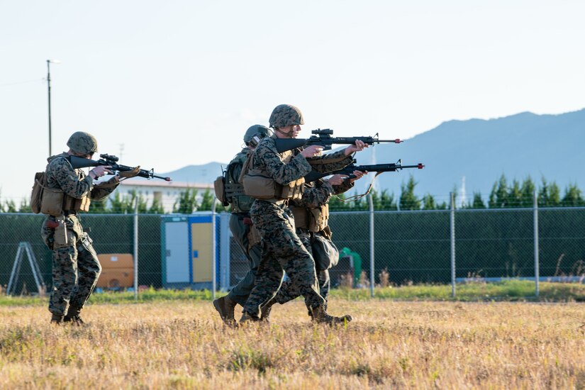 Marines aim weapons while walking in a field.