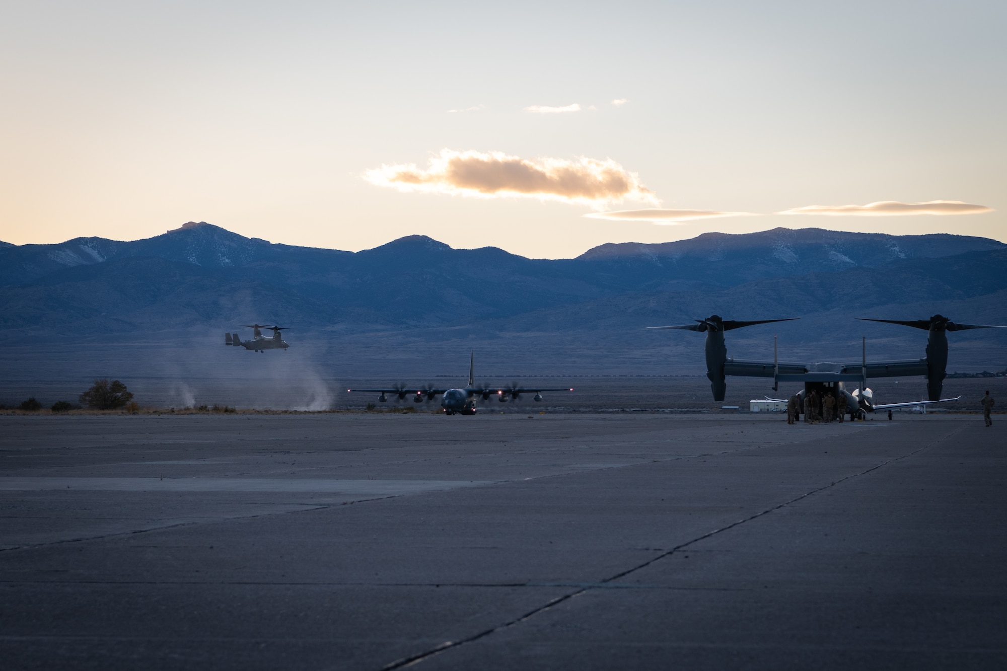 A CV-22 tiltrotor aircraft lands while an MC-130J Commando two aircraft taxis down a runway.
