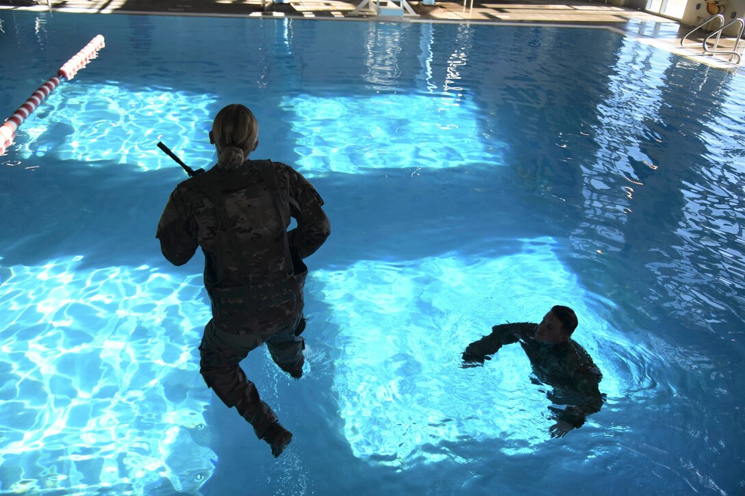 A soldier leaps into a pool while a fellow soldier floats in the water.