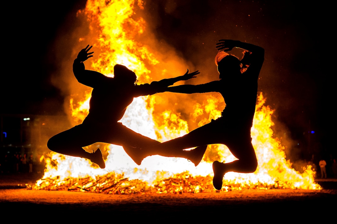 Air Force cadets jump in the air in front of a large bonfire.