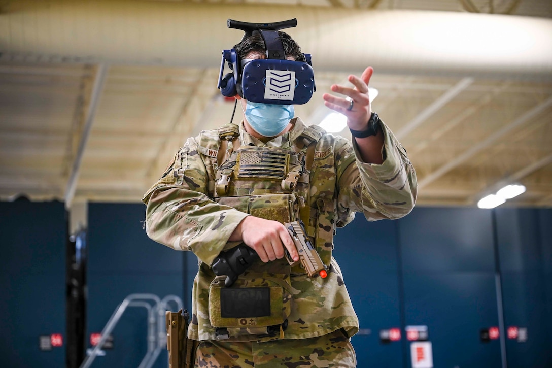 An airman wears virtual reality goggles while holding a weapon.