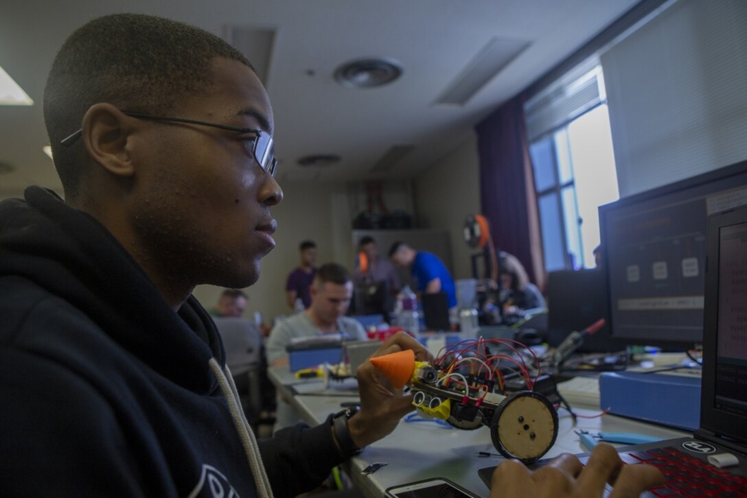 A man looks at a computer screen as he holds a piece of equipment in his left hand.