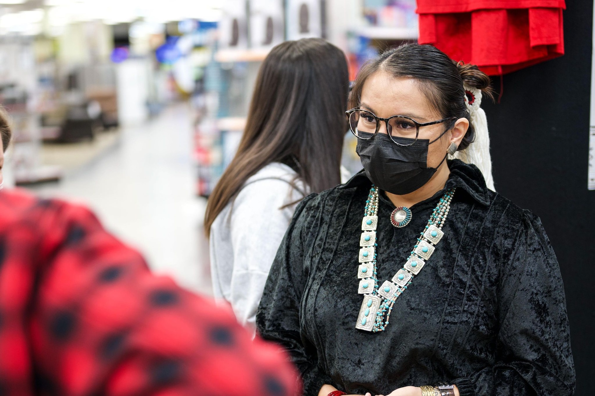 A woman in Native American regalia speaks with a man in a red flannel inside a department store setting