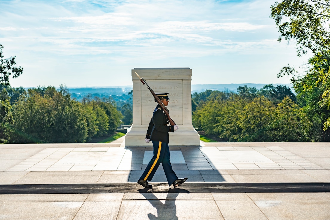 A soldier with a rifle walks along the black mat before the Tomb of the Unknown Soldier.