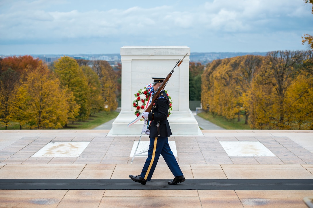 A soldier walks the mat in front of the Tomb of the Unknown Soldier carrying a rifle.