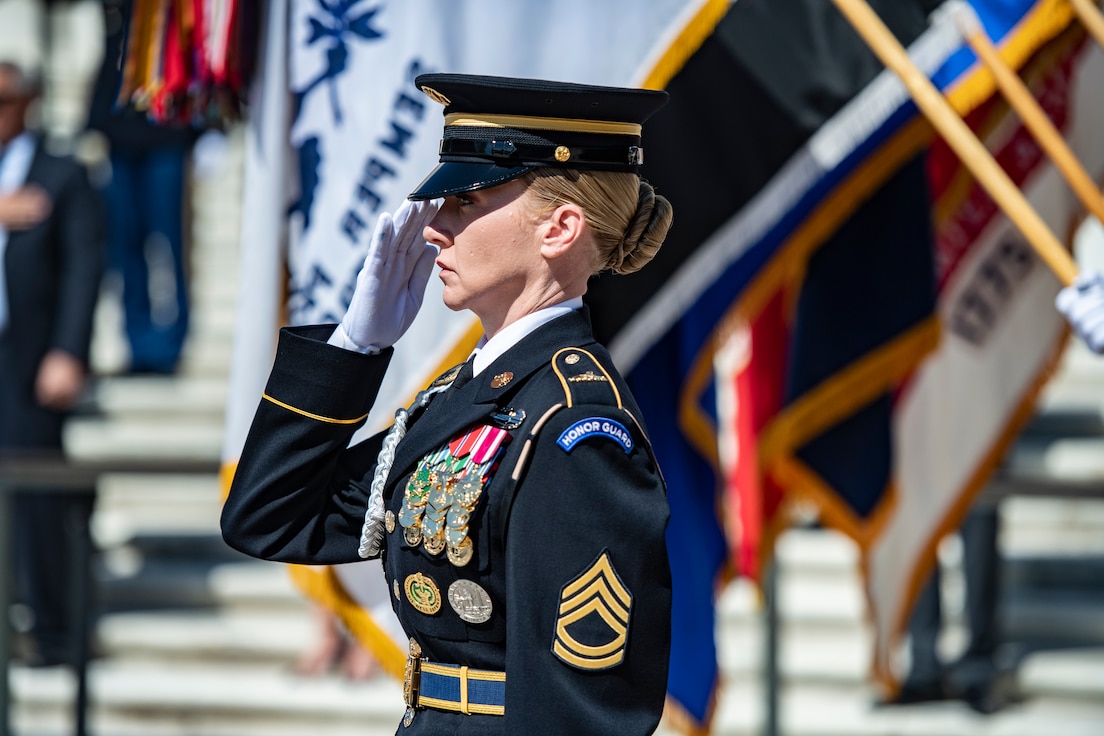 A soldier salutes in front of several flags.