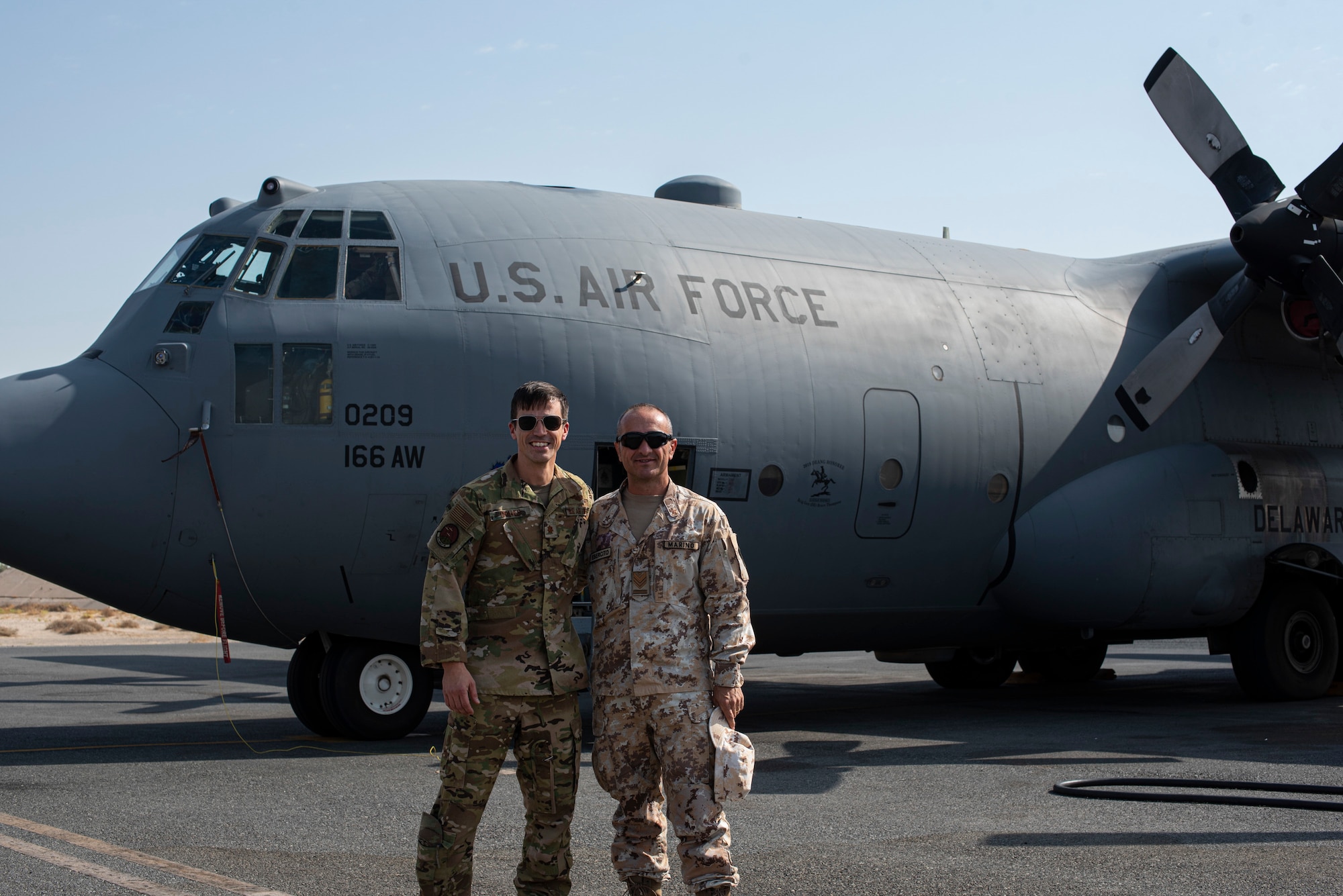 A USAF pilot and Italian Air Force member pose in front of a C-130H Hercules