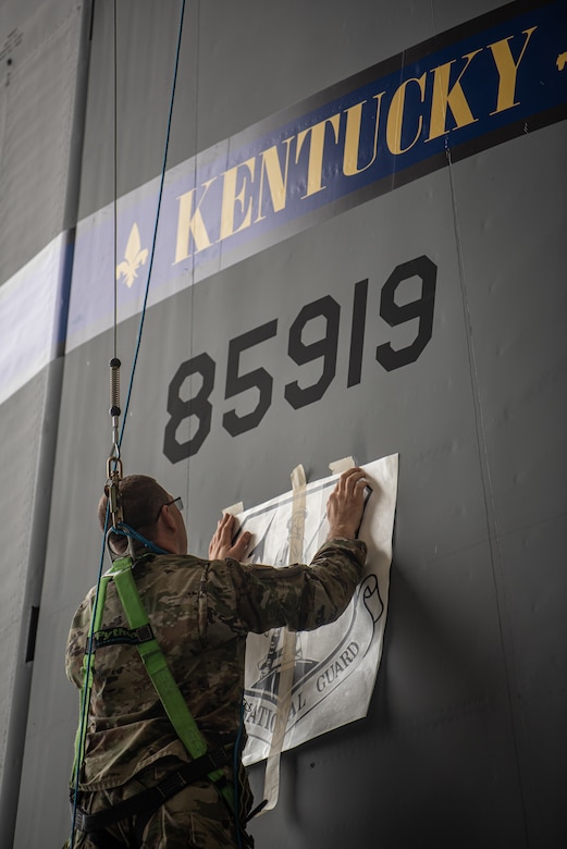 Master Sgt. Lee Stanley, aircraft structural repair shop chief for the 123rd Maintenance Group, applies a decal of the Air National Guard emblem to the tail of one of the Kentucky Air National Guard’s newly acquired C-130J Super Hercules aircraft at Channel Islands Air Guard Station in Port Hueneme, Calif., Nov. 4, 2021. The aircraft will be replacing the C-130H Hercules, which has been in service to the Kentucky Air National Guard since 1992. (U.S. Air National Guard photo by Tech. Sgt. Joshua Horton)