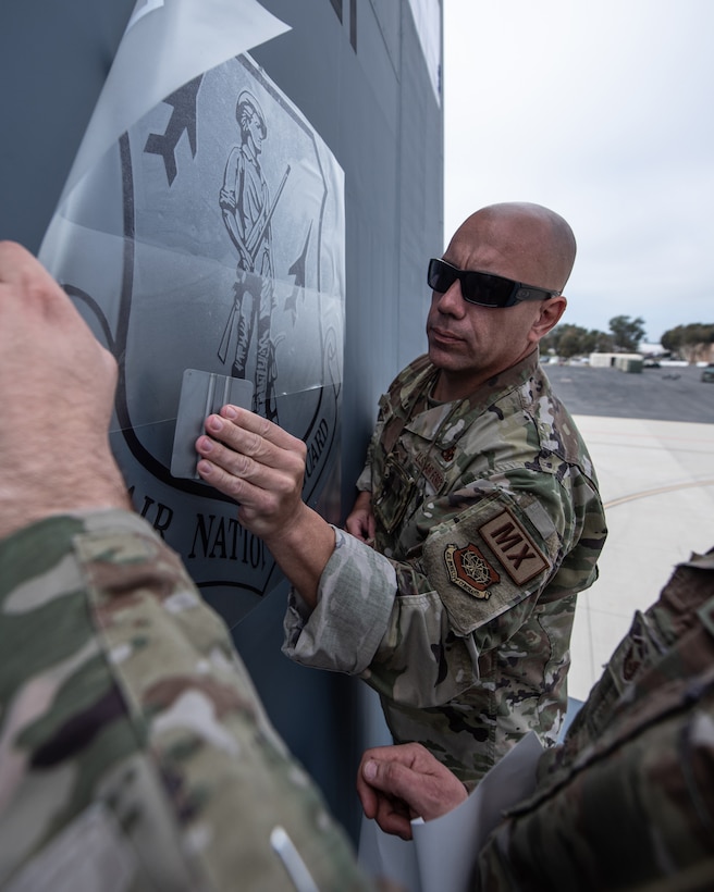 Chief Master Sgt. Tim Kenney, aircraft structural repair shop chief for the 123rd Maintenance Group, applies a decal of the Air National Guard emblem to the tail of one of the Kentucky Air National Guard’s newly acquired C-130J Super Hercules aircraft at Channel Islands Air Guard Station in Port Hueneme, Calif., Nov. 4, 2021. The aircraft will be replacing the C-130H Hercules, which has been in service to the Kentucky Air National Guard since 1992. (U.S. Air National Guard photo by Tech. Sgt. Joshua Horton)