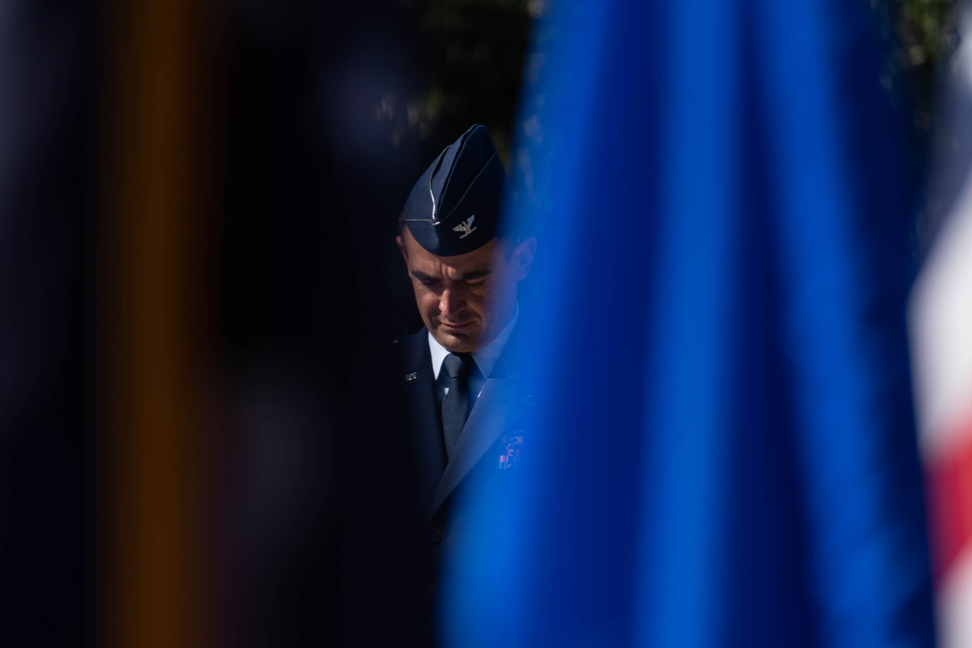 Col. Rubio stands between two flags with his head bowed.