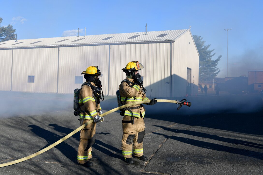 Airman Christopher Patrick and Senior Airman Jacob Parent, firefighters with the 104th Civil Engineer Squadron, lead a hose while putting out a simulated fire during a midpoint inspection on November 5, 2021 at Barnes Air National Guard Base, Massachusetts. Midpoint inspections are conducted to evaluate the wing’s capabilities to respond to threats in a contested, degraded, and operationally limited environment. (U.S. Air National Guard photo by Senior Airman Camille Lienau)