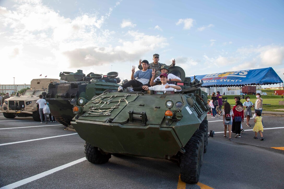 CAMP SCHWAB, OKINAWA, Japan – Okinawa residents and a U.S. Marine pose for a photo on top of a Light Armored Vehicle static display during an open-gate festival at Camp Schwab, Okinawa, Japan, Nov. 7, 2021. The festival was the first open-gate event hosted on Marine Corps installations in Okinawa in over a year due to COVID-19. (U.S. Marine Corps Photo by Matthew Manning)