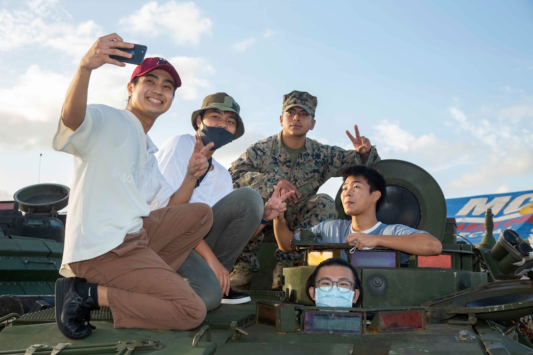 CAMP SCHWAB, OKINAWA, Japan – Okinawa residents and a U.S. Marine pose for a photo on top of a Light Armored Vehicle static display during an open-gate festival at Camp Schwab, Okinawa, Japan, Nov. 7, 2021. The festival was the first open-gate event hosted on Marine Corps installations in Okinawa in over a year due to COVID-19. (U.S. Marine Corps Photo by Matthew Manning)