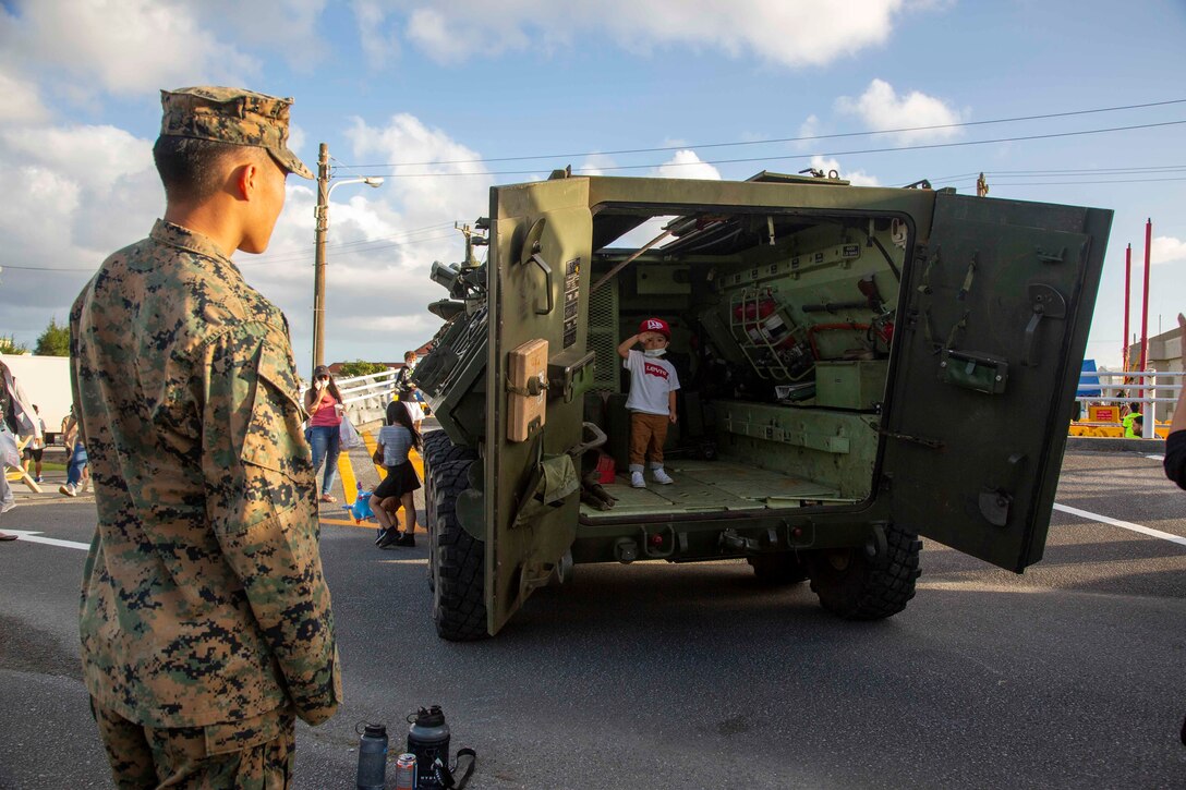 CAMP SCHWAB, OKINAWA, Japan – A U.S. Marine looks on as a child poses for a photo inside a Light Armored Vehicle static display during an open-gate festival at Camp Schwab, Okinawa, Japan, Nov. 7, 2021. The festival was the first open-gate event hosted on Marine Corps installations in Okinawa in over a year due to COVID-19. (U.S. Marine Corps Photo by Matthew Manning)