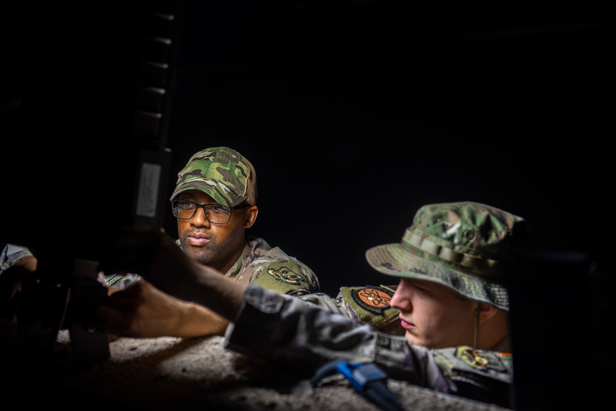 photo of two U.S. Air Force Airmen setting up LED light outside in the dark