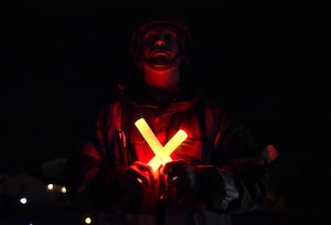 An F-16 Fighting Falcon crew chief assigned to the 31st Maintenance Group wears Mission Oriented Protective Posture gear while holding marshaling glow sticks to signal an F-16 at Aviano Air Base, Italy, Nov. 4, 2021. The 31st Fighter Wing conducted exercise Fighting Wyvern, a base defense exercise, Nov. 1-5, and provided Airmen the opportunity to train for realistic situations they may face in a real-world combat environment. (U.S. Air Force photo by Senior Airman Brooke Moeder)