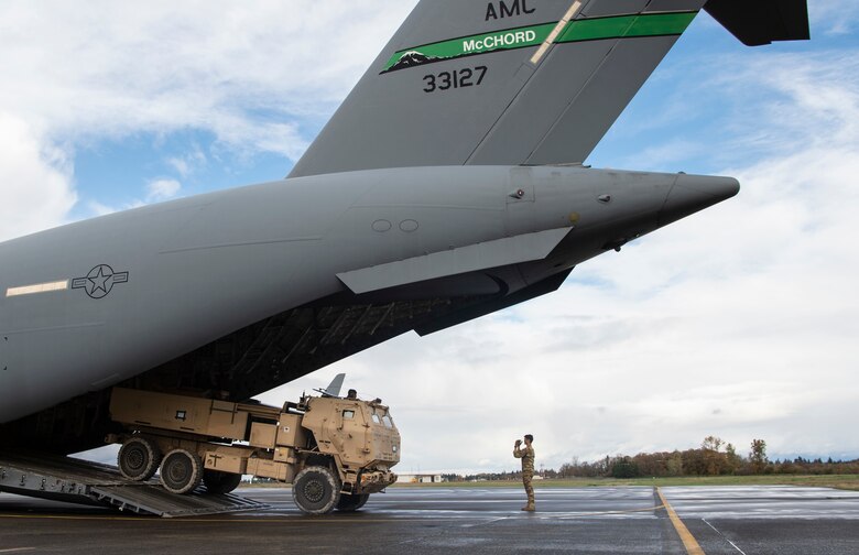 U.S. Air Force Senior Airman Keoni Gibson, 8th Airlift Squadron loadmaster, marshals a U.S. Army M142 High Mobility Rocket System (HIMARS) off a C-17 Globemaster III during Exercise Rainier War 21B at Joint Base Lewis-McChord, Washington, Nov. 6, 2021. Rainier War 21B exercises and evaluates the wing’s ability to employ the force and their ability to perform during wartime and/or contingency taskings in a high-intensity, wartime contested, degraded and operationally limited environment while supporting the contingency operations against a near-peer adversary in the U.S. Indo-Pacific Command area of responsibility. (U.S. Air Force photo by Staff Sgt. Tryphena Mayhugh)