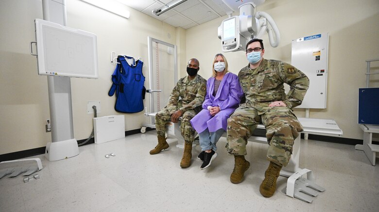 Left to right, Tech. Sgt. Quincy Shay, Rhonda Janroy and Staff Sgt. Anthony Hiser, sitting on an x-ray table.