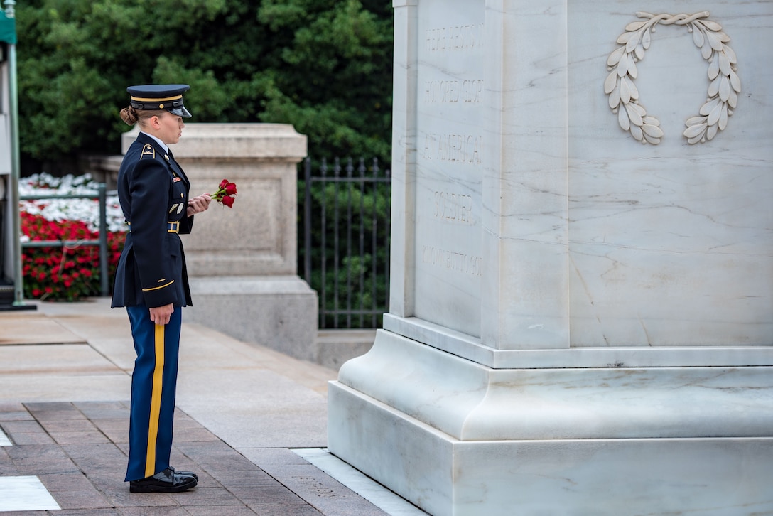 A soldier stands and holds a rose in front of a tomb.
