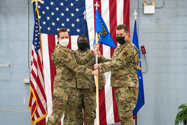 A woman wearing an Air Force uniform hands a unit flag to a man in uniform.