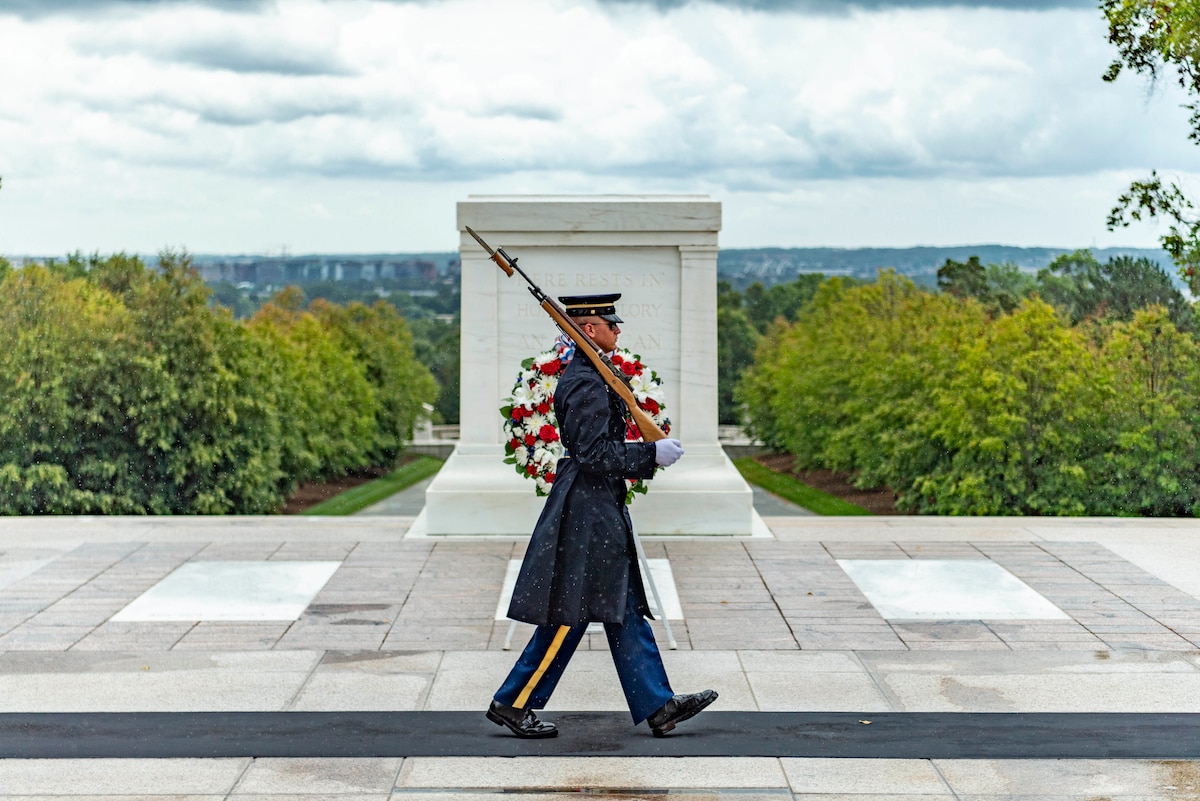 A soldier walks on a mat in front of a marble tomb.