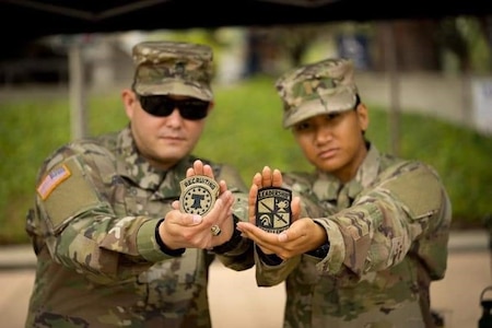 Two Soldiers in uniform holding up their unit patches.