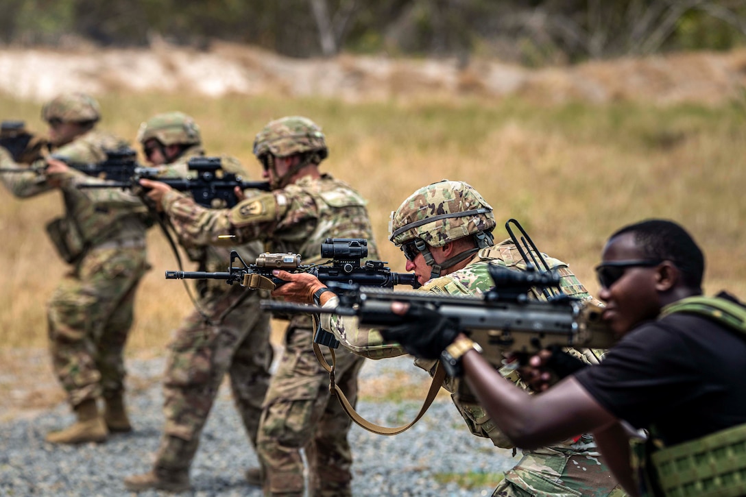 U.S. and Kenyan troops fire weapons in a field.