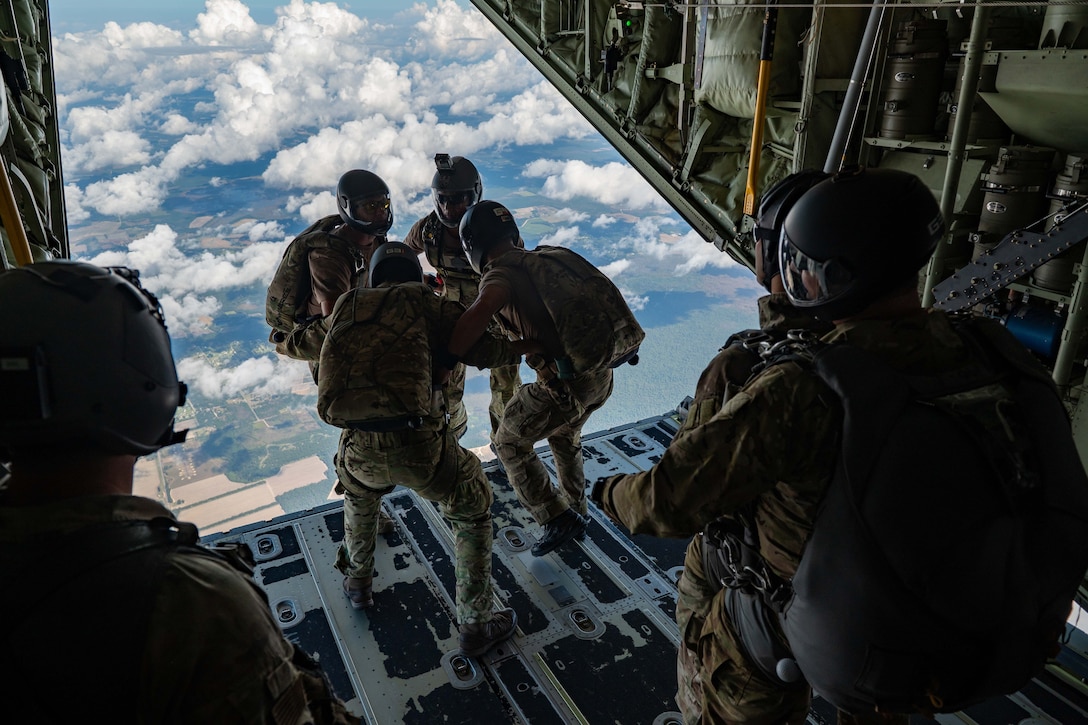 Airmen prepare to jump from the back of an aircraft.