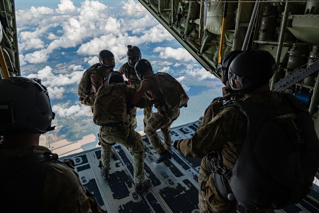 Airmen prepare to jump from the back of an aircraft.